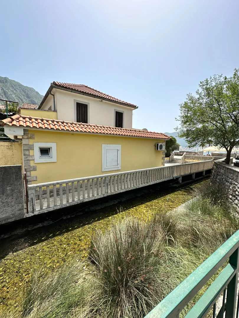 Exterior view of a house with a yellow facade and a terrace by a stream.