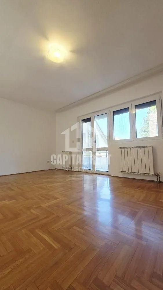 Empty room with parquet flooring and large windows letting in natural light.