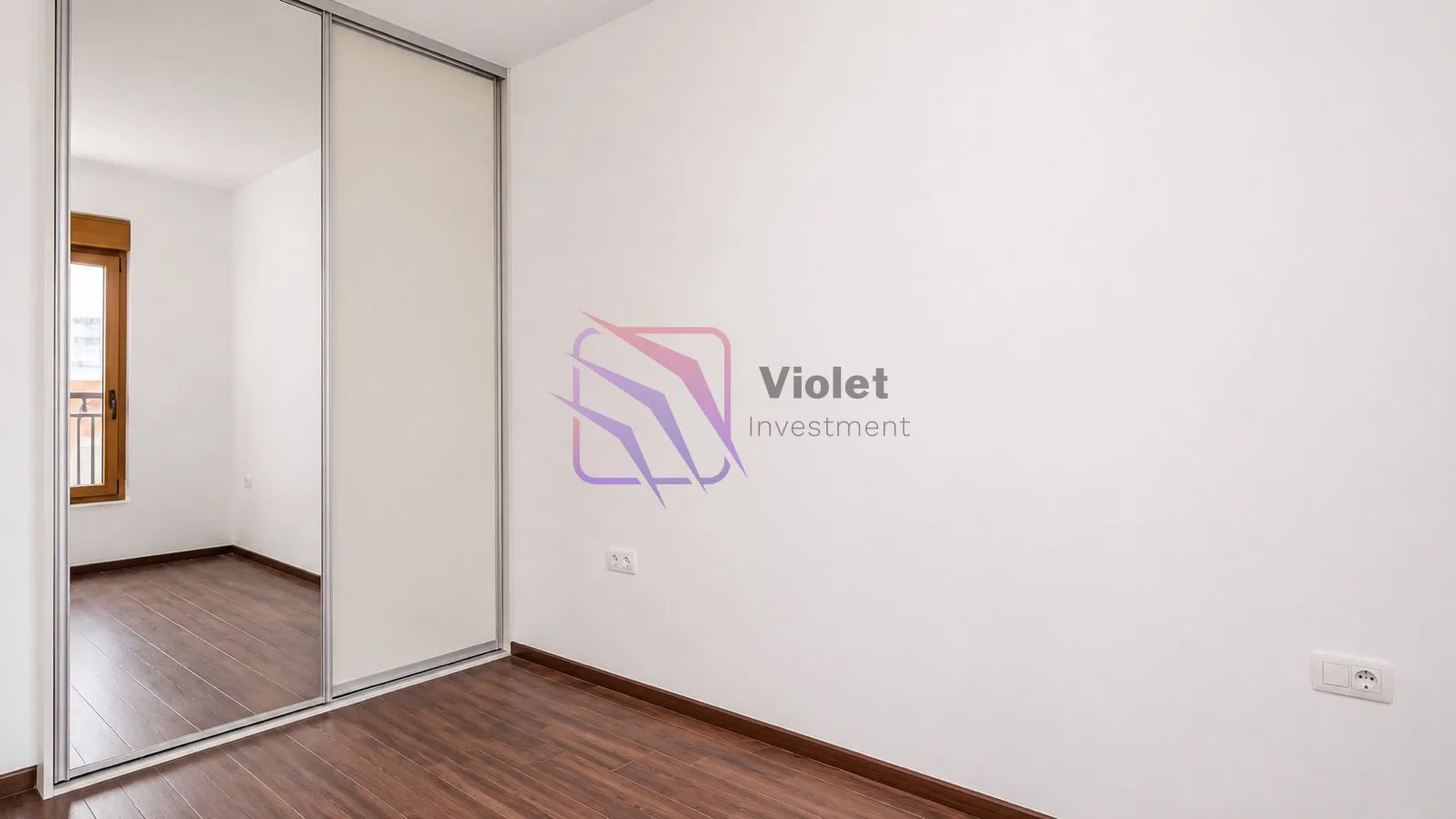 A room with white walls, dark wooden flooring, and a large built-in wardrobe with sliding doors.