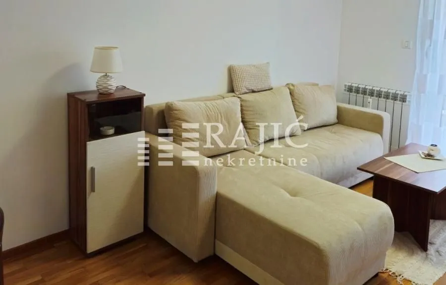 Living room with a sectional sofa, coffee table, and a small cabinet with a lamp.
