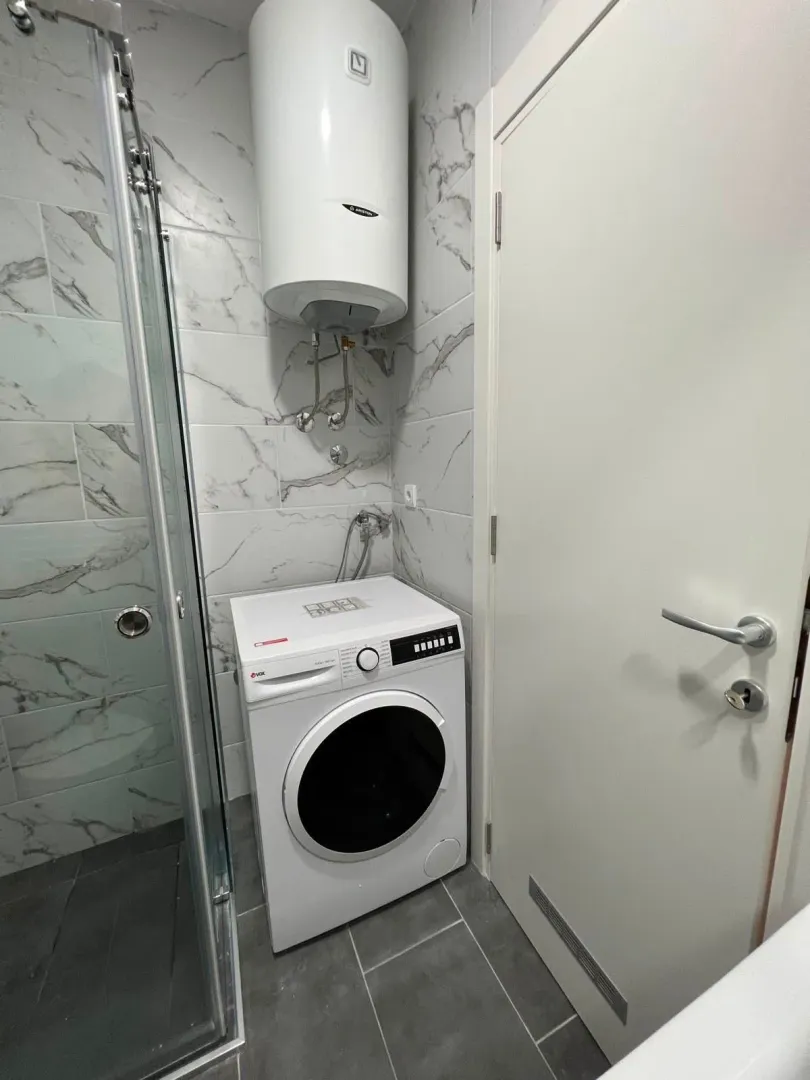 View of the bathroom with a shower cabin, water heater, and washing machine.