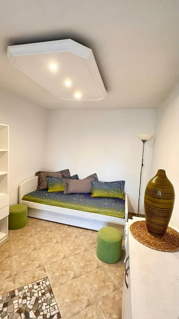 Smaller bedroom with a bed, stools, and a decorative vase.