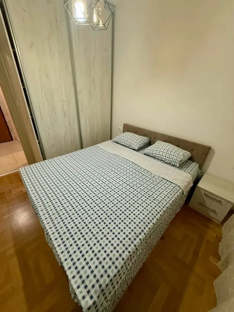 Namještena spavaća soba sa bračnim krevetom, plakarom i noćnim stočićem.
