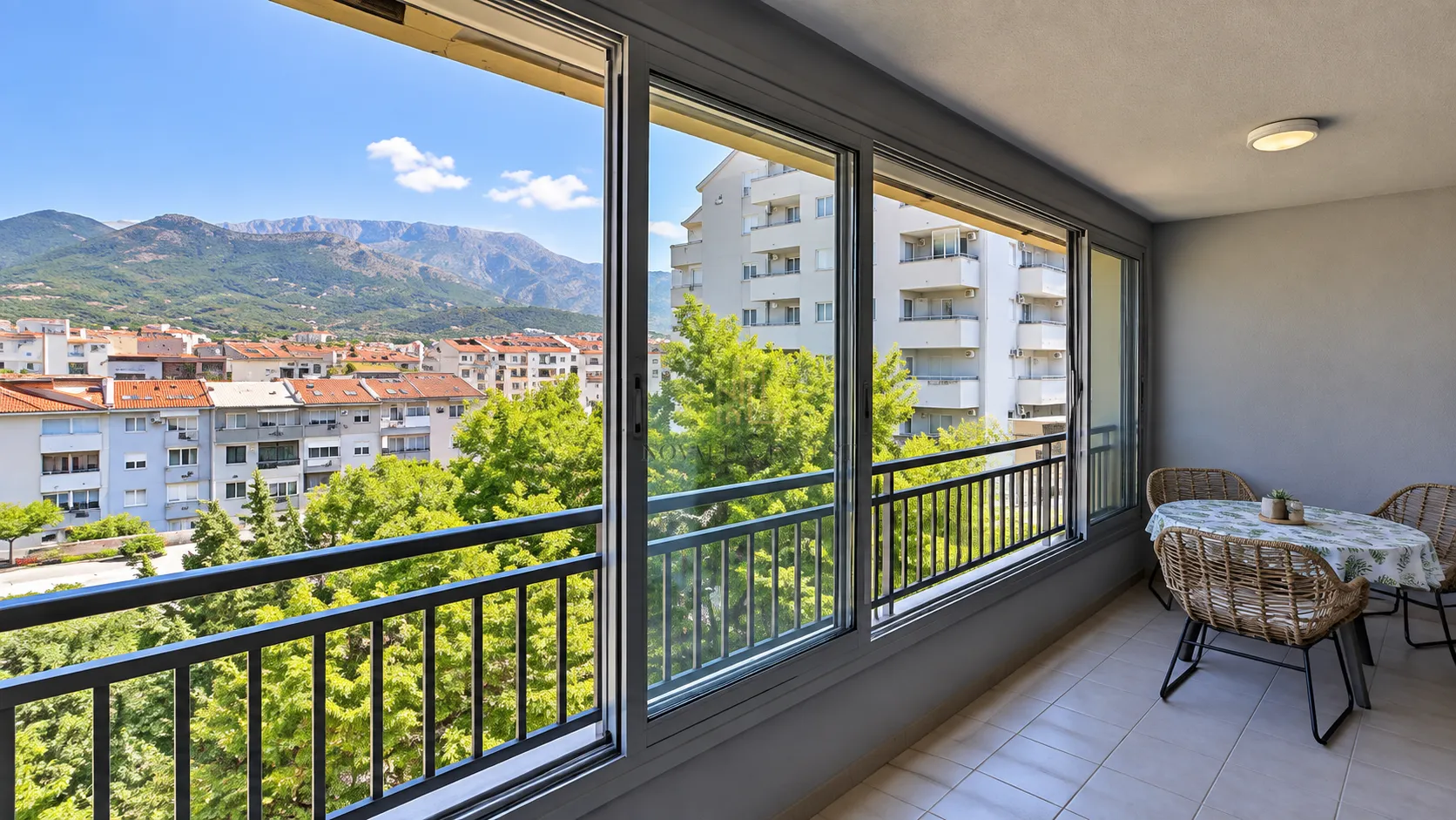 Enclosed balcony with a dining table and a view of the city and mountains.