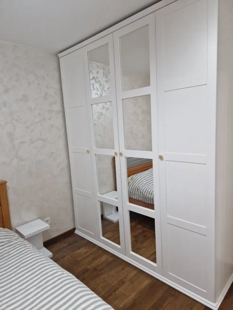 Spavaća soba sa velikim bijelim ormarom sa ogledalima.