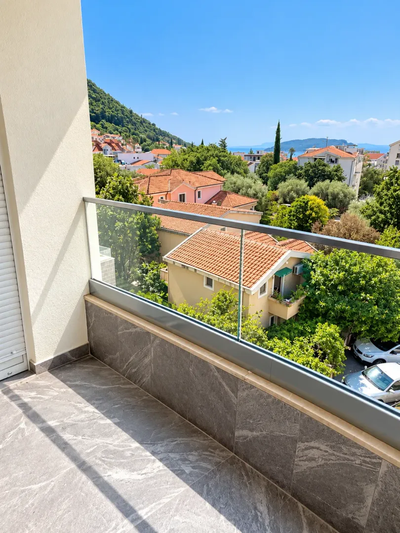 Modern balcony with a glass railing and a view of the neighborhood and greenery.