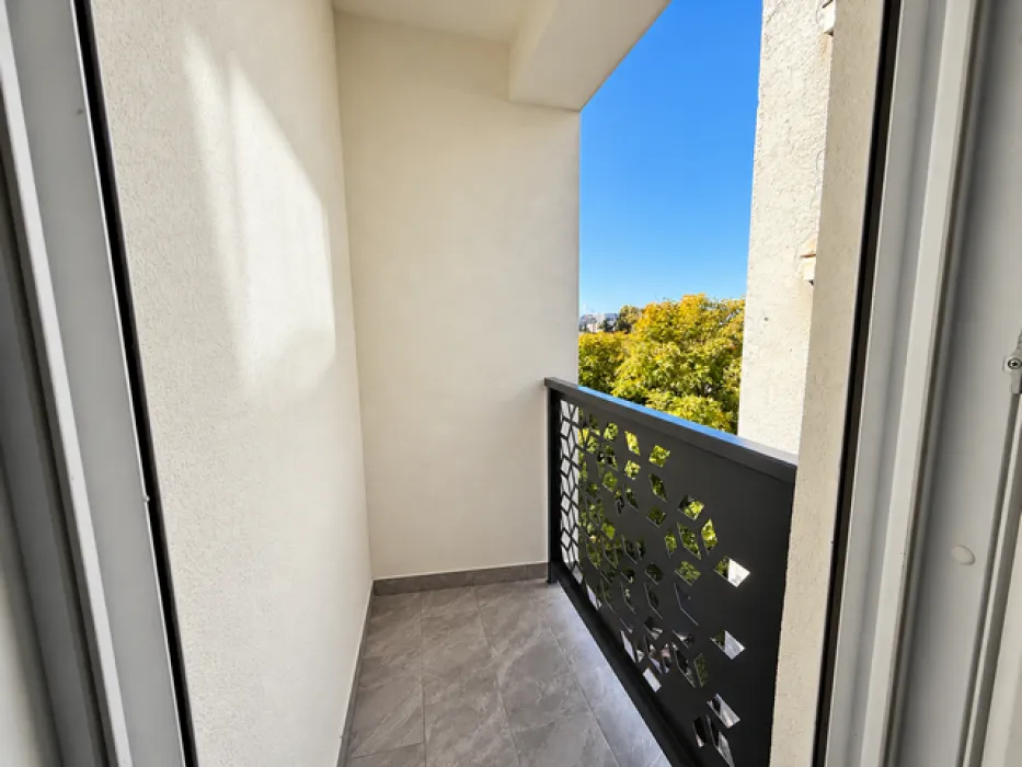 A small covered balcony with a dark metal railing and a view of greenery.