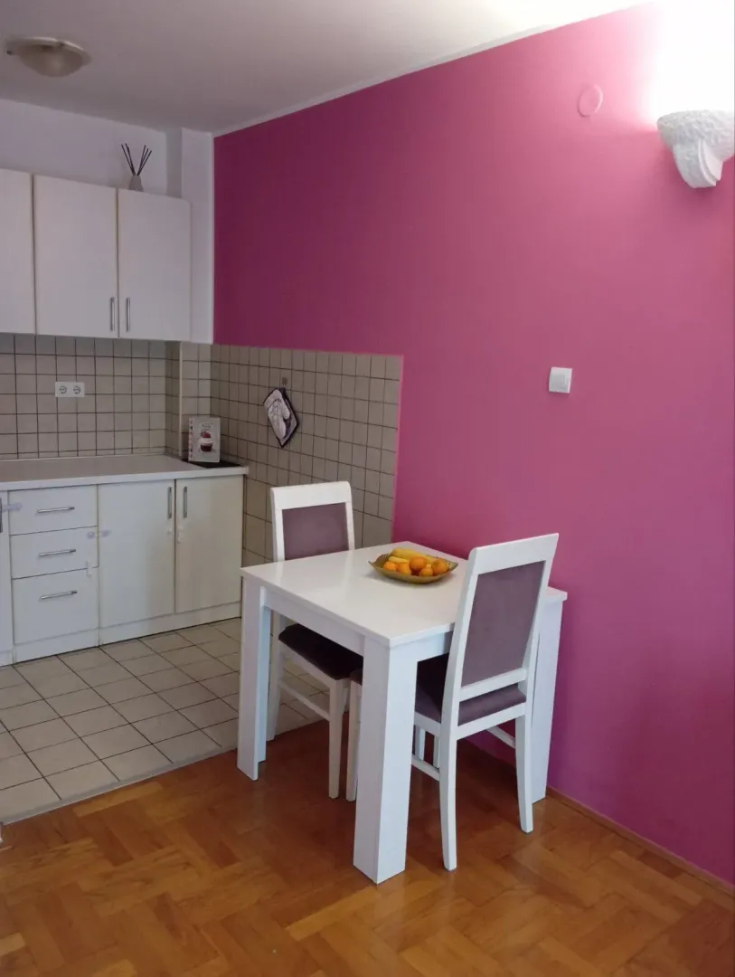 Kuhinja sa malim trpezarijskim stolom pored upečatljivog ružičastog zida.
