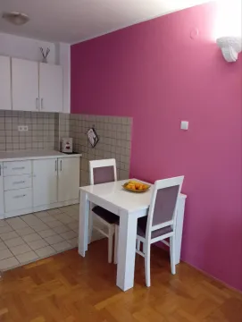 Kuhinja sa malim trpezarijskim stolom pored upečatljivog ružičastog zida. - image 4