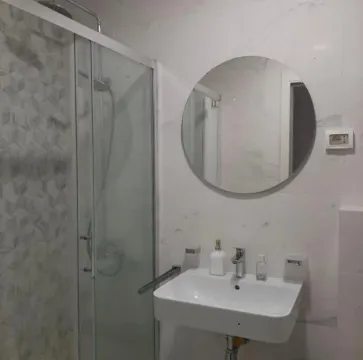 Modernly equipped bathroom with a walk-in shower, washbasin, and a round mirror. - image 8