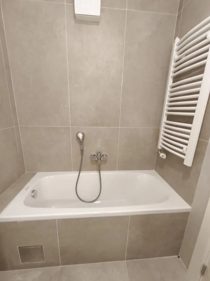 Kupatilo opremljeno kadom i belim radijatorom sušačem peškira na zidu.