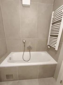 Kupatilo opremljeno kadom i belim radijatorom sušačem peškira na zidu. - image 7