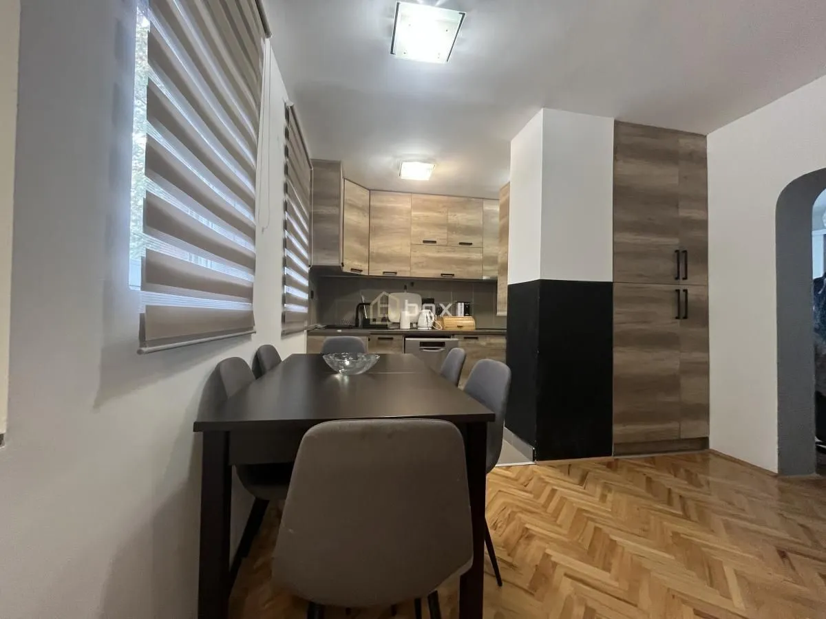 Kitchen with a dining table and chairs, wooden cabinetry, and windows with roller blinds.