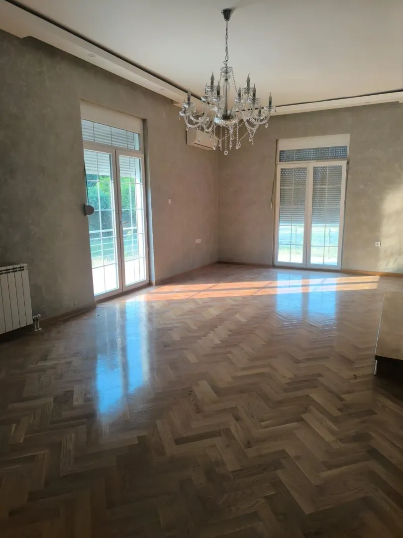 Empty living room with parquet flooring, a chandelier, and two balcony doors.