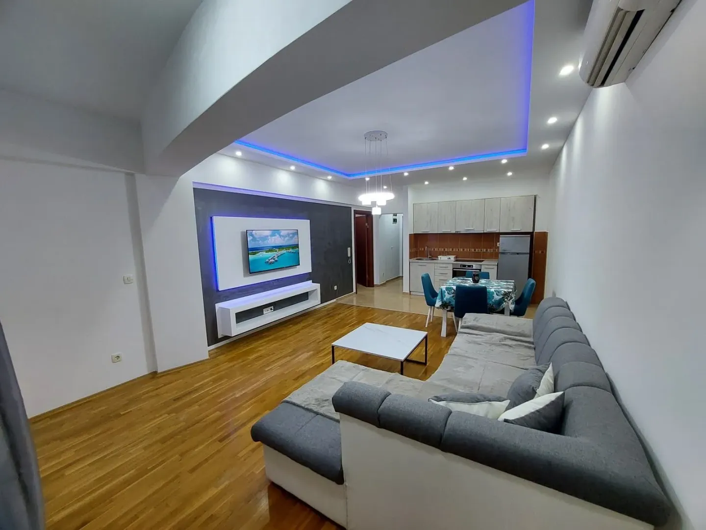 Modern living room with a sofa, TV unit, and dining area in the background.