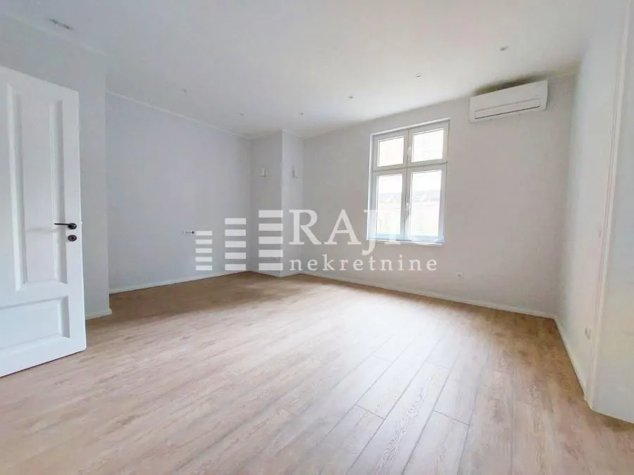 Empty bright room with hardwood flooring and air conditioning unit.