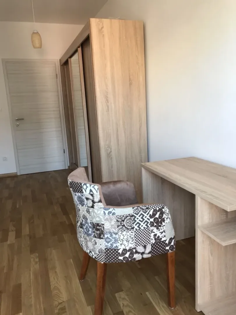 A room featuring a wooden desk, a patterned armchair, and a large wardrobe.