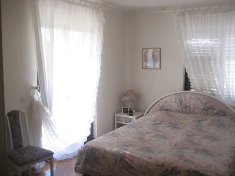 A bedroom featuring a double bed, a nightstand, and windows with white curtains. - image 4