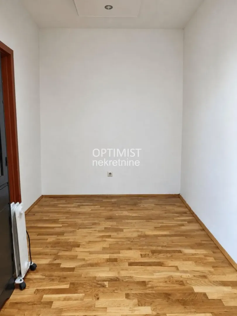 Prazna soba sa drvenim parketom i belim zidovima.
