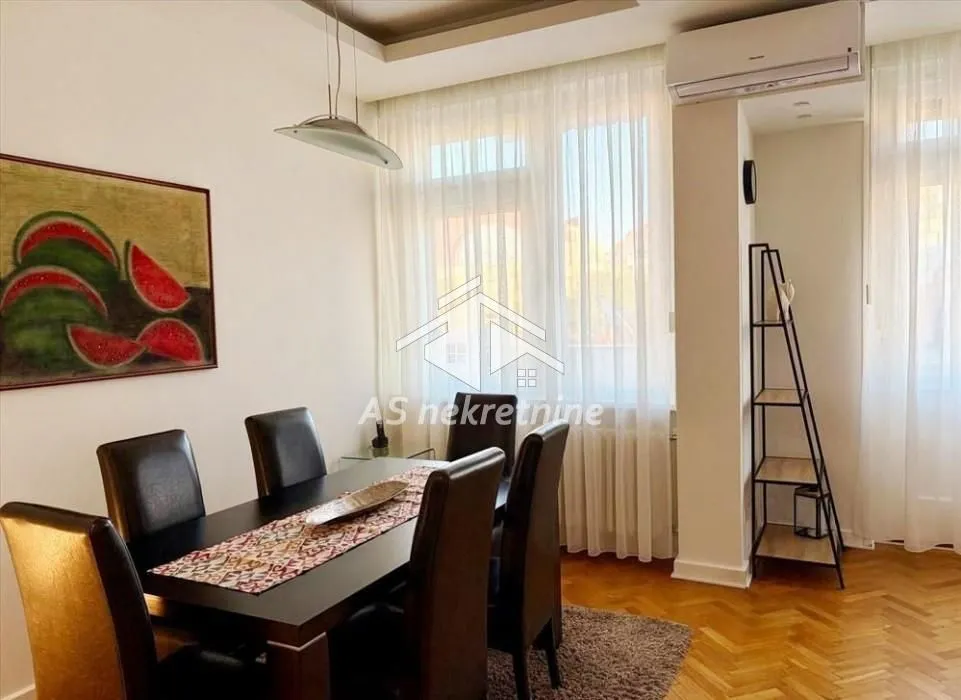 Dining area with a dining table and chairs, next to a window with light curtains.