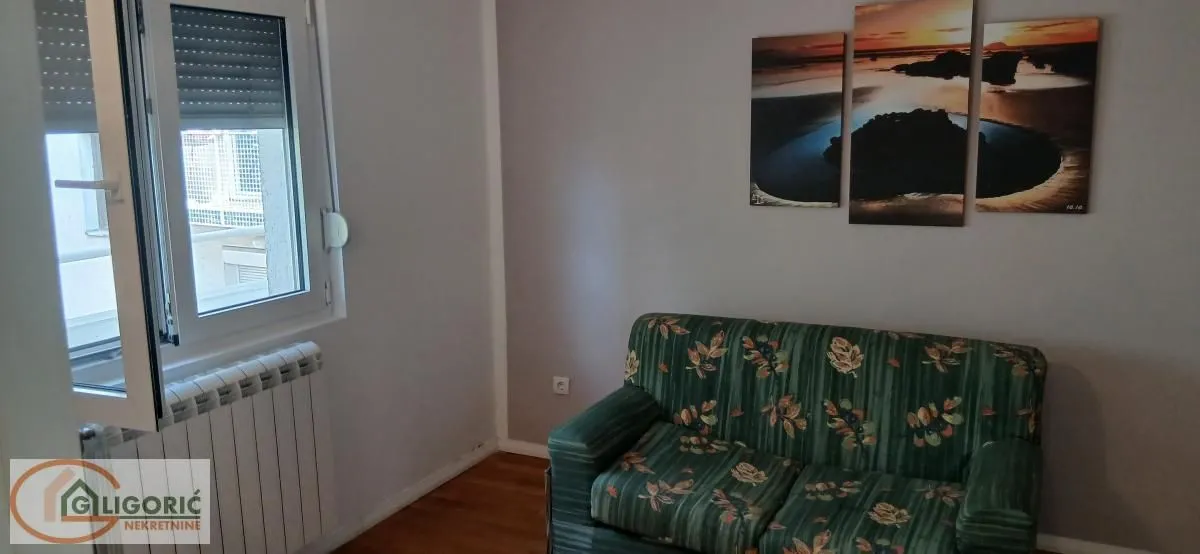 Manja dnevna soba sa zelenim kaučem i prozorom.