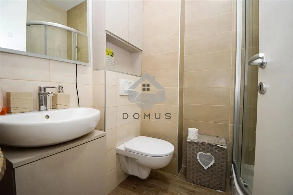 Compact bathroom with a shower cabin, washbasin, and toilet in beige tones.