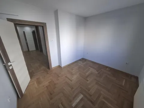 Prazna soba sa drvenim parketom i otvorenim vratima prema hodniku. - image 11
