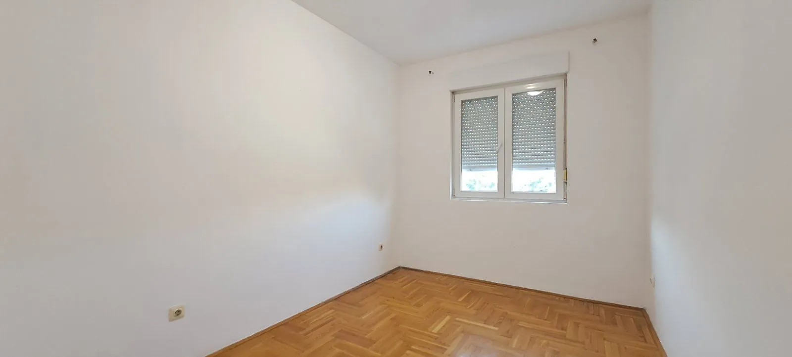 Prazna soba sa bijelim zidovima i parketom na podu.