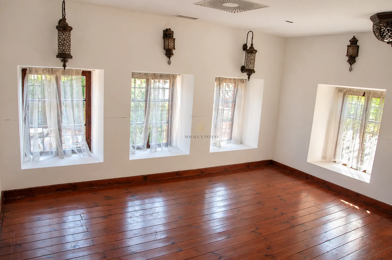 Empty room with wooden flooring, white walls, and decorative wall lamps.