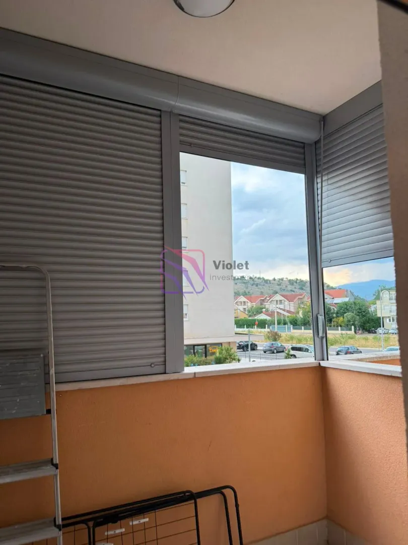 Enclosed balcony space with roller shutters and a view of surrounding buildings and neighborhood.