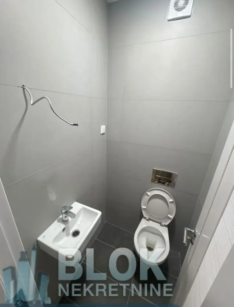 Manje kupatilo sa sivim pločicama, umivaonikom i šoljom.