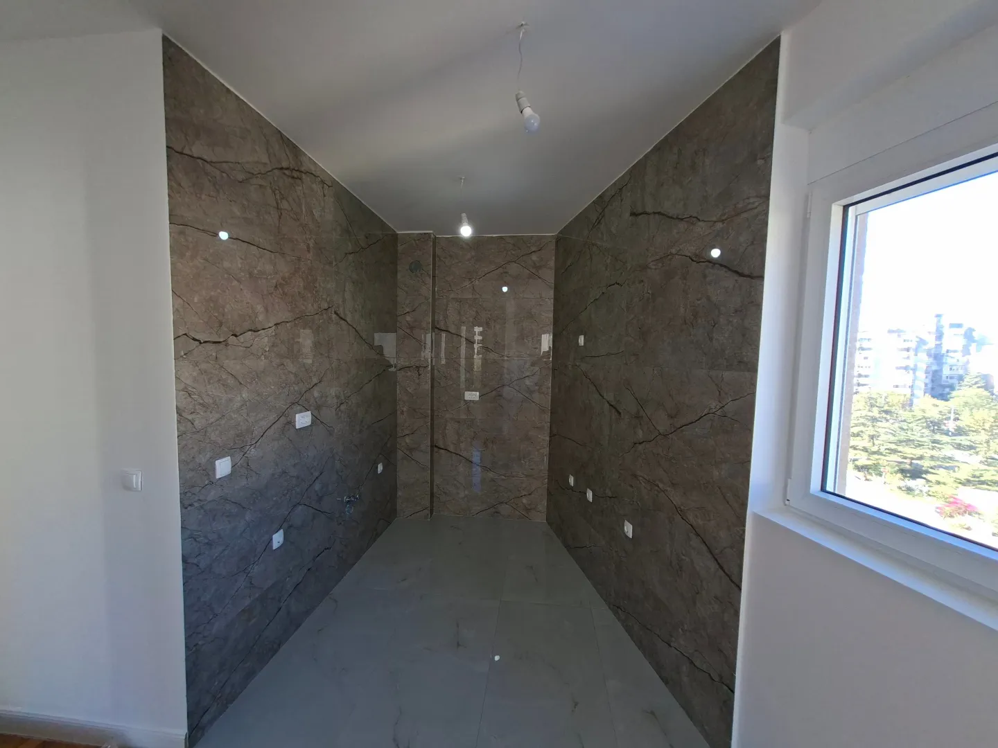 Empty kitchen with marble-effect ceramic tiles on the walls and a window.