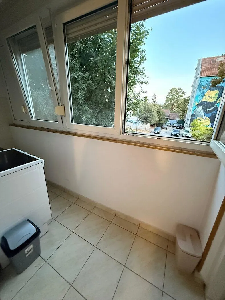 Zastakljeni balkon sa keramičkim pločicama i pogledom na ulicu.