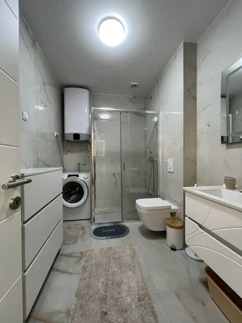 Moderne kupatilo sa tuš kabinom, umivaonikom i veš mašinom.