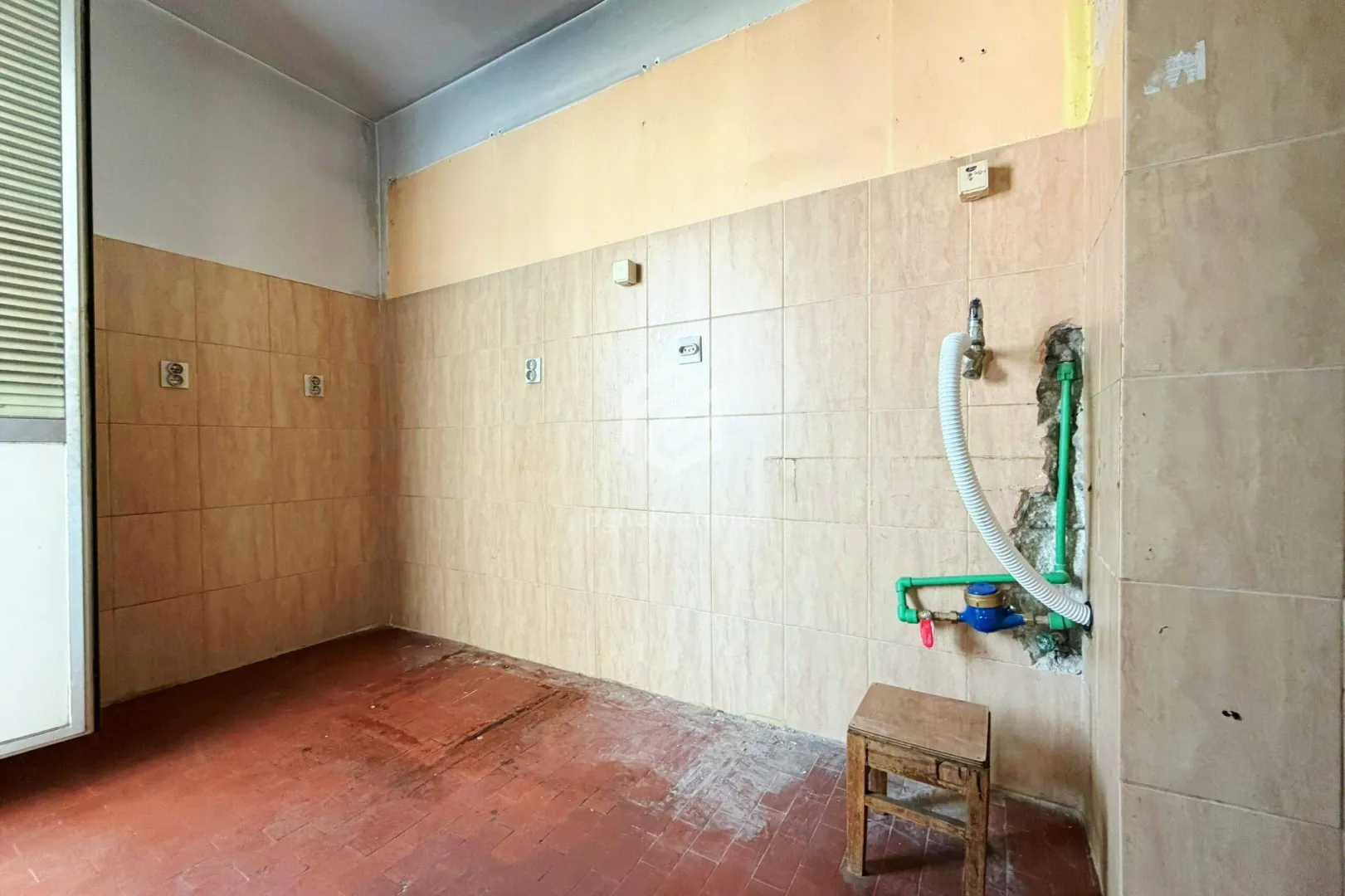 Prazna prostorija sa pločicama na zidu i instalacijama za kuhinju.
