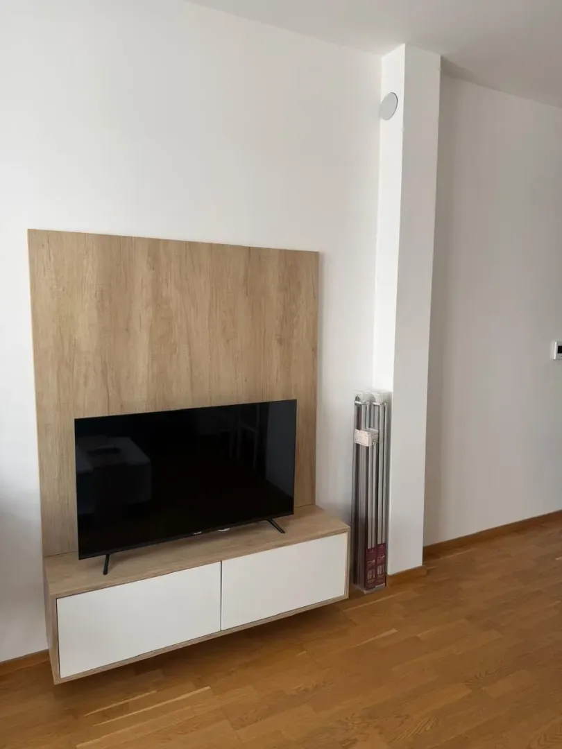 Dnevna soba sa TV komodom i drvenim panelom na zidu.
