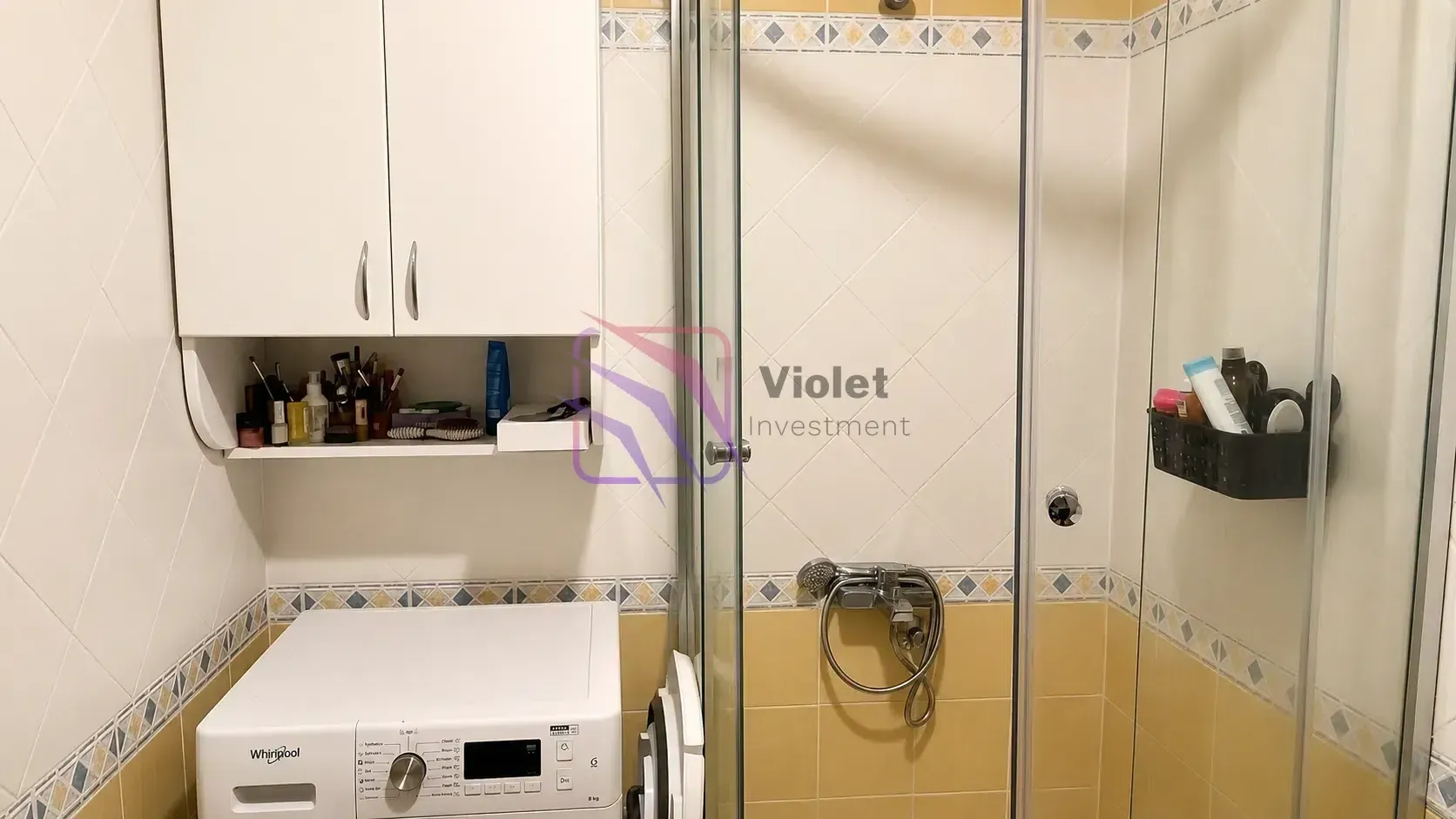 Kupatilo sa tuš kabinom, veš mašinom i bijelim ormarićem.