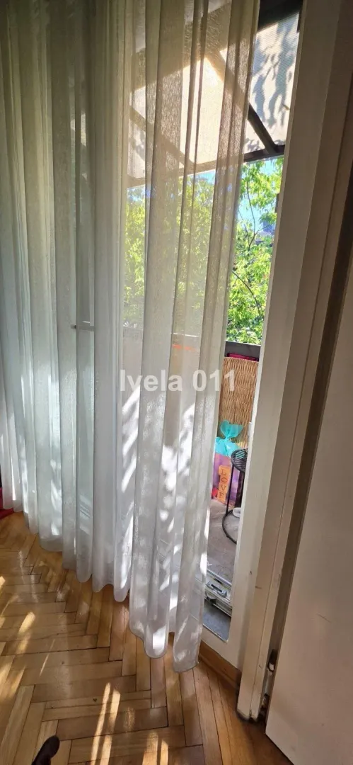 Balkonska vrata sa svetlim zavesama i pogledom na zelenilo.