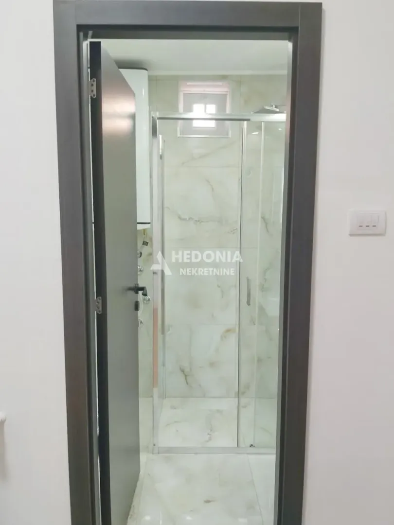 Pogled kroz otvorena vrata na kupatilo sa tuš kabinom.