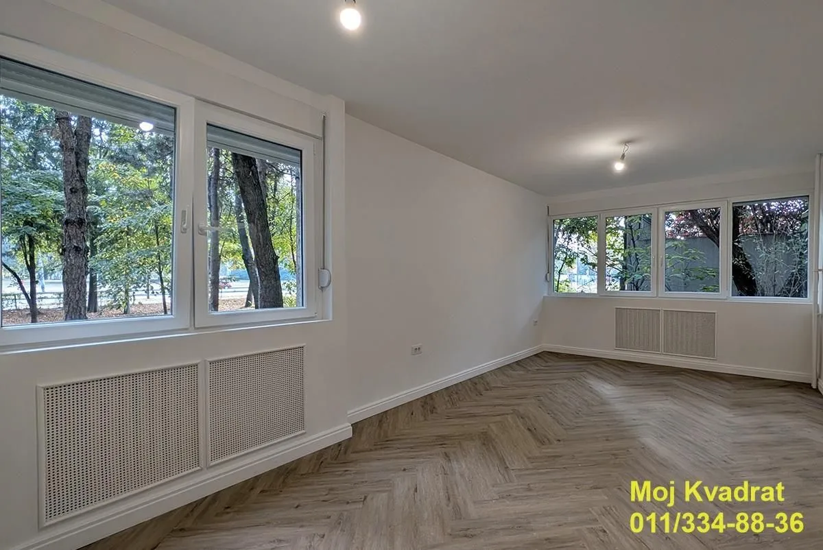 Prazna soba sa belim zidovima, parketom i više prozora.