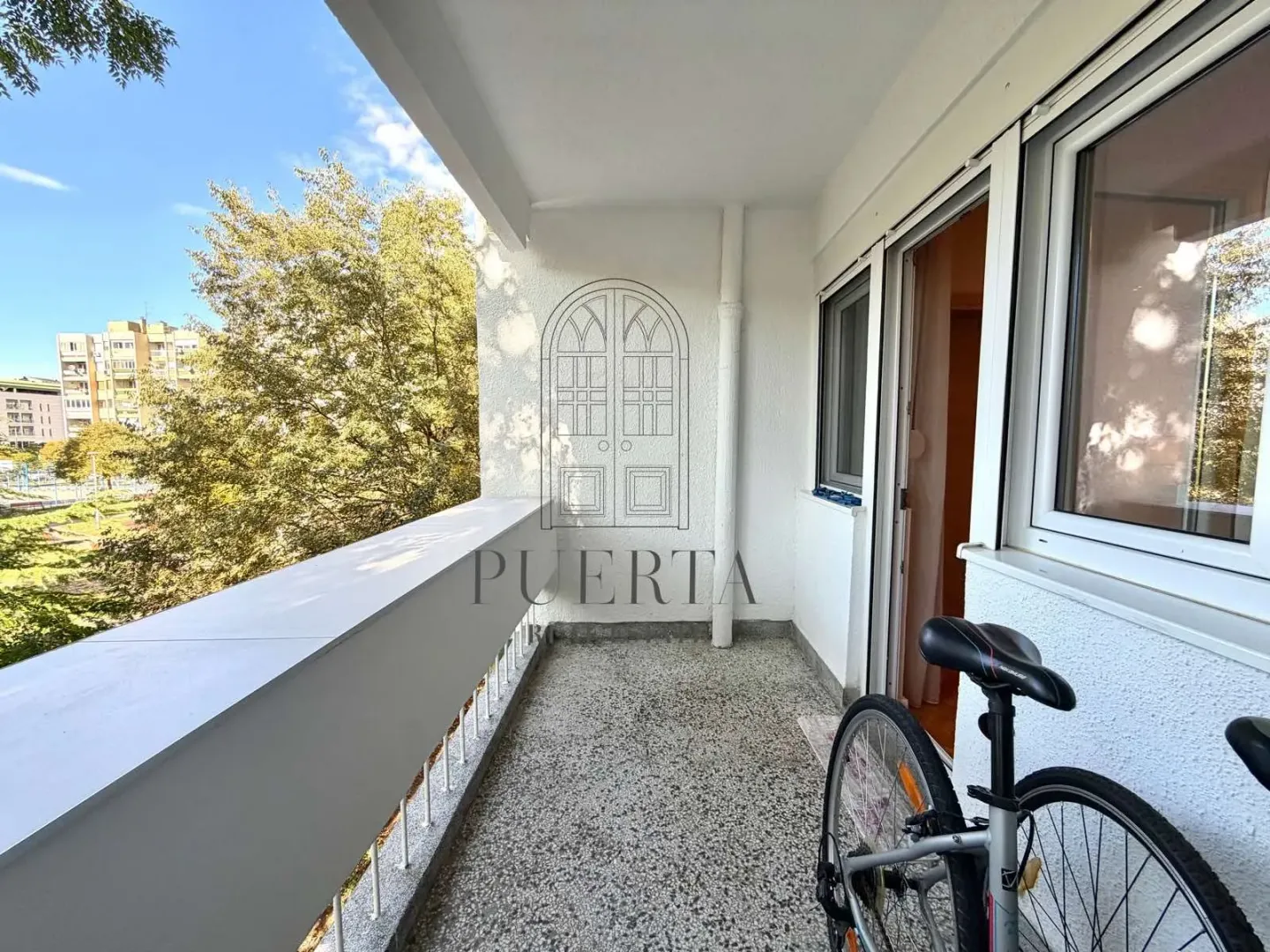 Natkriveni balkon sa pogledom na okolne zgrade i biciklom u uglu.