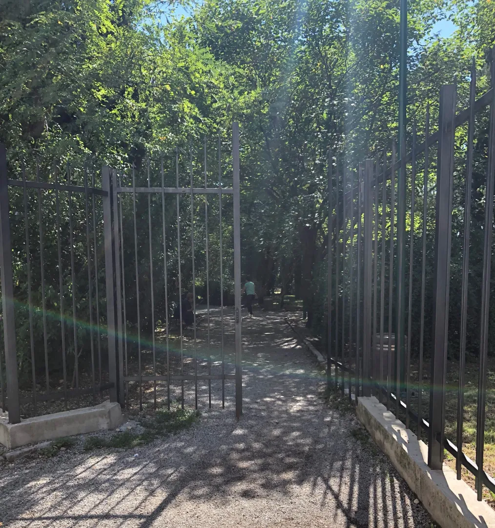 Dvorište sa metalnom kapijom i stazom okruženom zelenilom.