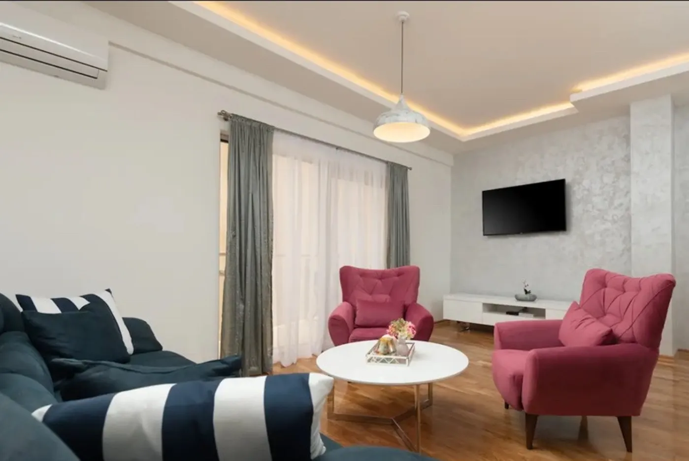 Moderna dnevna soba sa garniturom, foteljama i televizorom.