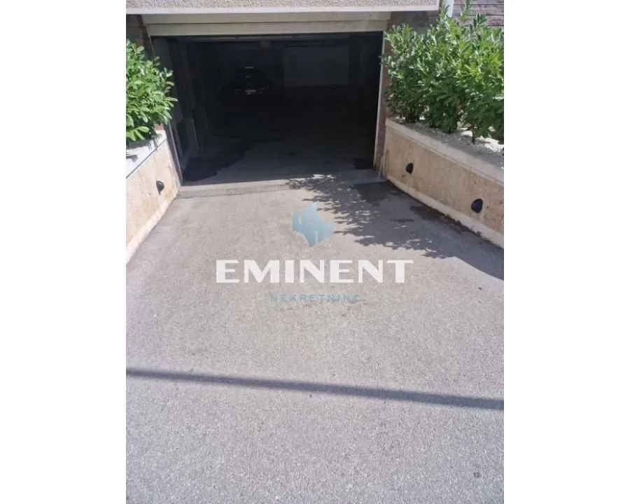 Driveway with garage entrance and landscaped greenery on the sides.