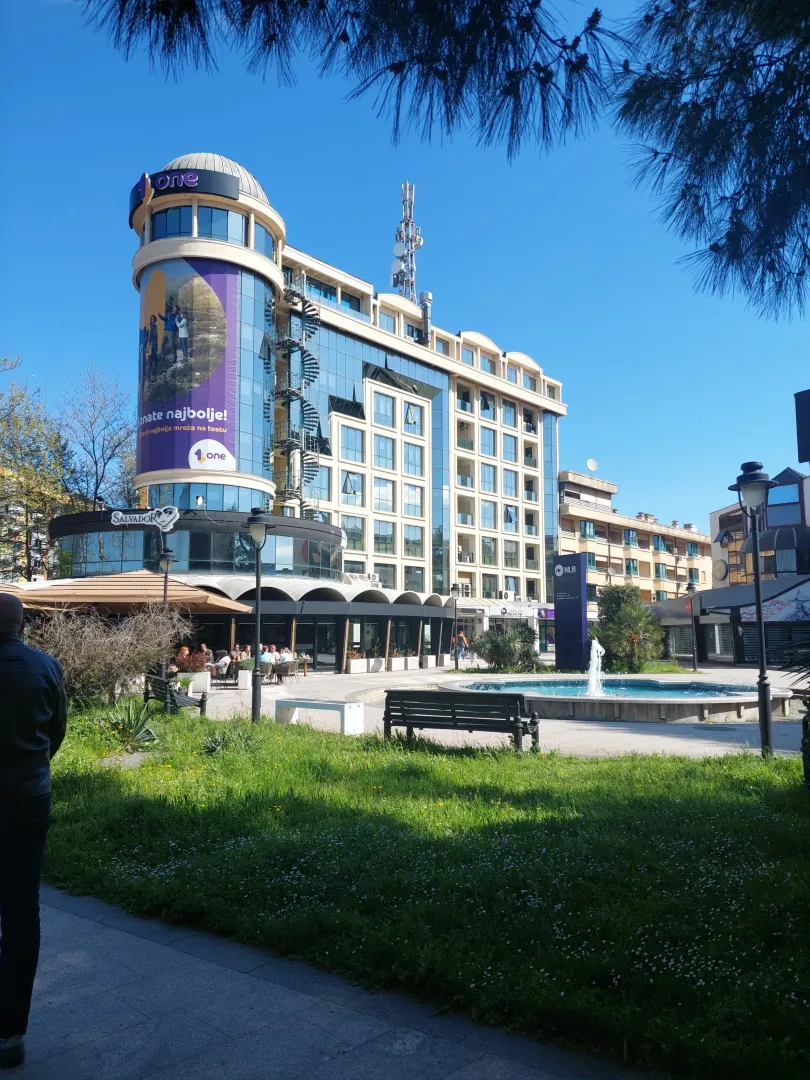 View of a modern commercial and residential building with a square and a fountain in the foreground.