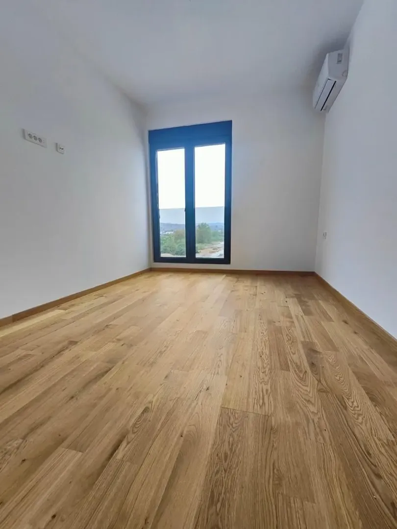 Empty room with wooden flooring, white walls, and a window.