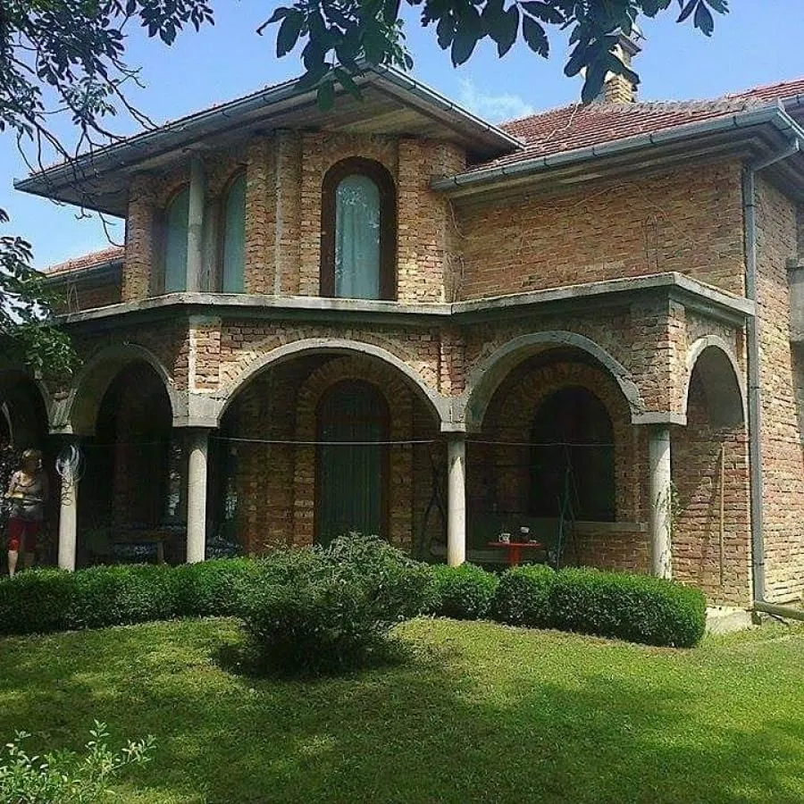 Spoljašnji izgled kuće od cigle sa tremom i uređenim dvorištem.