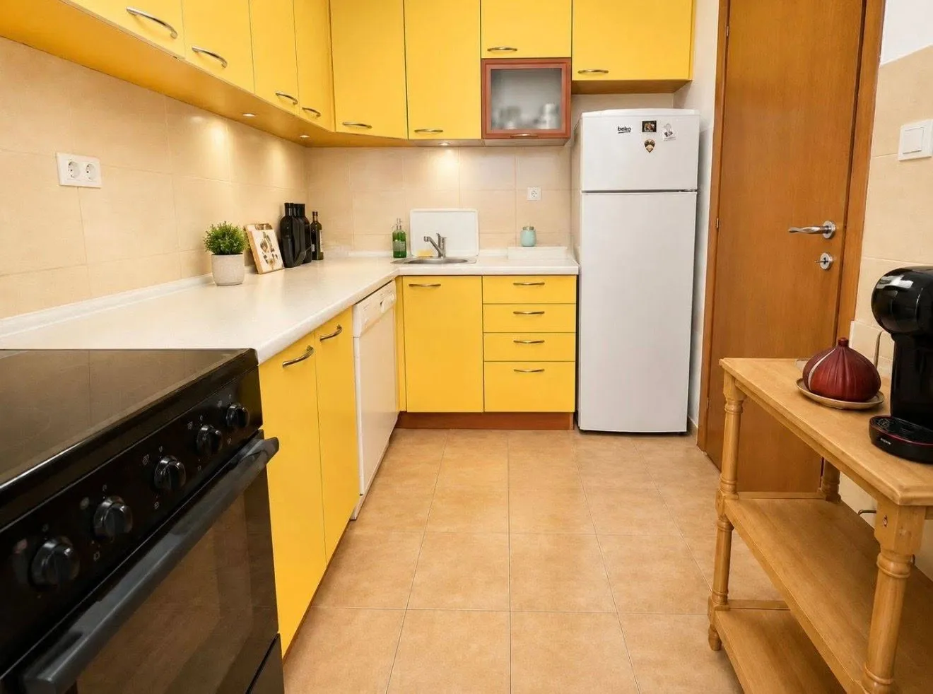 Kuhinja sa žutim elementima i bijelom radnom površinom.