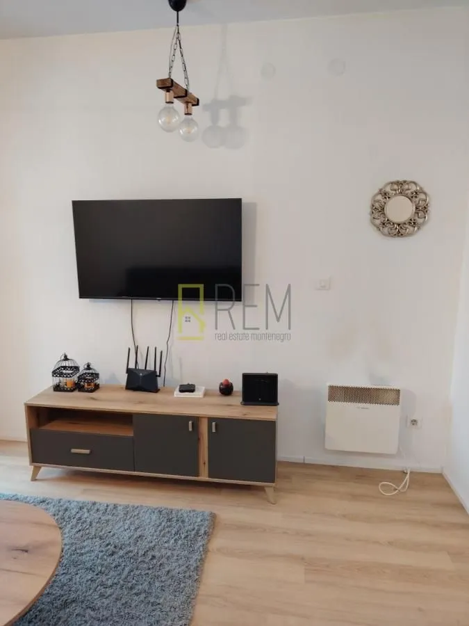 Dnevni boravak sa TV komodom i televizorom na zidu.