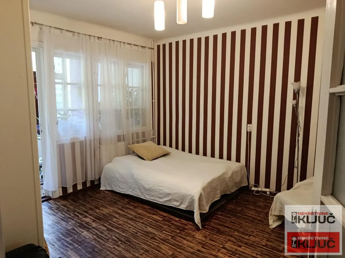Nameštena spavaća soba sa krevetom i prugastim tapetama na zidu.